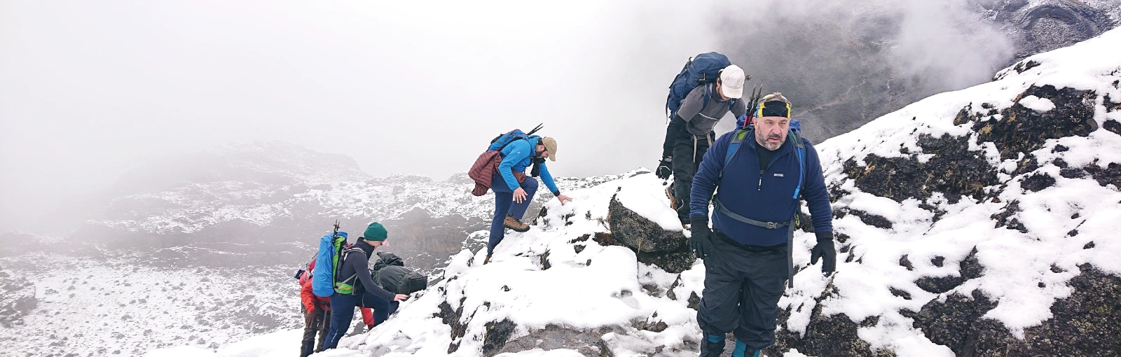 A group of hikers climbing the Barranco Wall on Mount Kilimanjaro with snow on the rocks